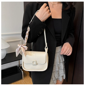 Detail of cream white crossbody bag with decorative silk scarf on shoulder strap