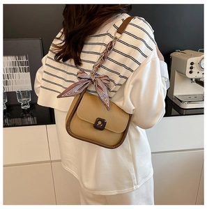 Detail of khaki shoulder bag with brown trim and decorative silk scarf on strap
