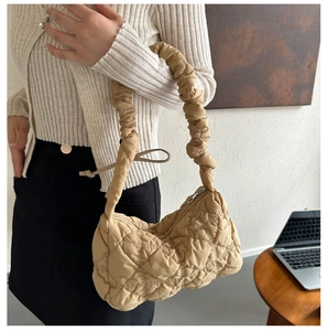 Detail of soft quilted cloud bag with ruched shoulder strap worn by a model in a room