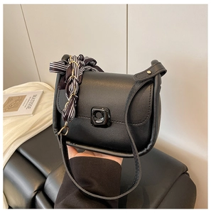 Detail of black semi-circular crossbody bag featuring striped silk scarf on the strap