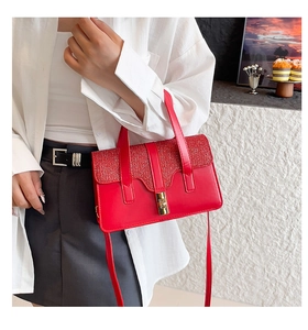 Close-up of red leather handbag featuring a glittery sequin flap and gold metal buckle
