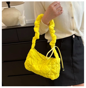 Detail of a bright yellow quilted bubble cloud bag with pleated strap worn by a model