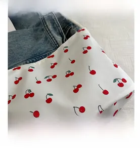 Detail of white nylon bucket bag featuring a vibrant red cherry print pattern
