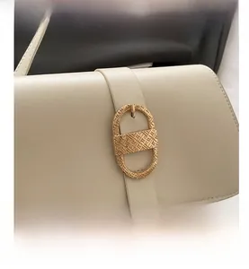 Detailed view of cream-colored shoulder bag featuring a textured oval golden buckle clasp