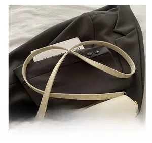 Close-up of cream shoulder bag with golden magnetic buckle and adjustable strap on a blazer