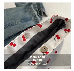 Close-up of silver magnetic metal clasp and cherry print on white nylon tote bag