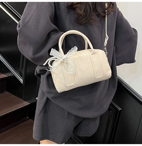 Détail du sac Boston crème avec nœud en dentelle et chaîne perlée sur une tenue grise