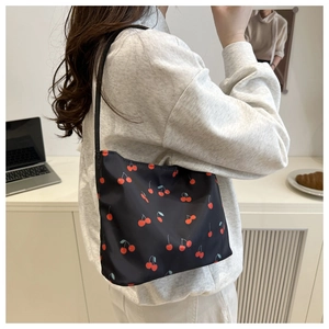 Close-up of black nylon shoulder bag with cherry print on a table with a laptop