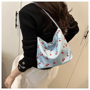Blue shoulder bag with red cherry pattern worn by a model in casual knitwear