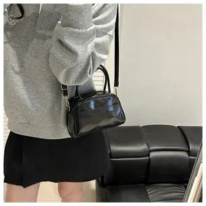 Detailansicht der schwarzen Lackhandtasche mit goldenen Beschlägen und Schultergurt