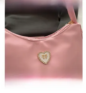 Detail view of pink crescent bag showing heart-shaped rhinestone and gold bow decor