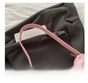 Detailed view of pink glossy underarm bag with heart jewel detail on grey suit jacket