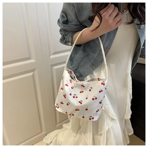 Detail view of large white canvas tote bag with vibrant red cherry patterns and shoulder strap