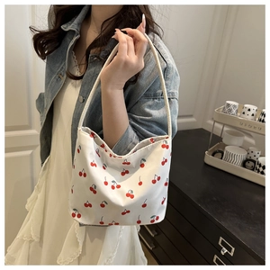 Detail of white canvas tote bag with red cherry print worn on shoulder by model