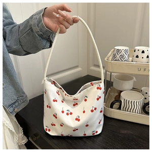 Detail view of a white canvas hobo bag with red cherry print and rope shoulder strap