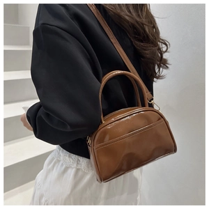 Detail einer dunkelbraunen Glanztasche mit goldenen Beschlägen und Schultergurt