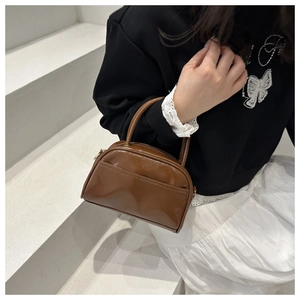 Detail einer braunen Lackleder-Handtasche mit glänzendem Finish und Doppelgriffen