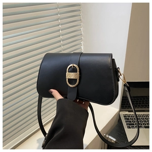 Detail view of a black leather shoulder bag featuring a textured gold oval metal buckle
