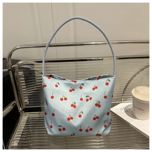 Detail of light blue shoulder bag with red cherry print on a minimalist metal bench