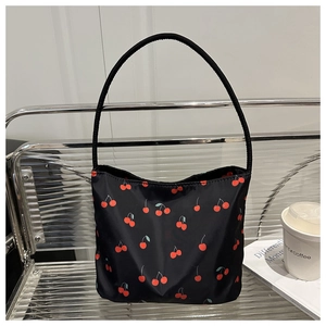 Close-up of black tote bag with red cherry print and slender shoulder strap on shelf