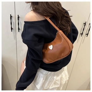 Brown faux leather underarm bag with silver heart metal charm shown on model's shoulder