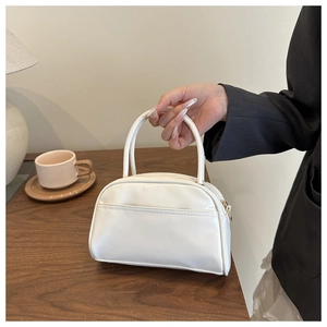 Minimalistische weiße Handtasche mit Doppelgriffen auf einem warmen Holztisch im Innenraum