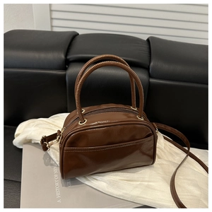 Detailansicht der glänzenden dunkelbraunen Mini-Henkeltasche auf weißem Stoff
