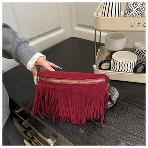 Detail of burgundy fringe crossbody bag with bohemian patterned strap on a counter