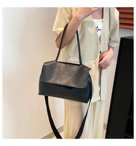 Detail of minimalist black leather tote bag with thick fabric shoulder strap on model