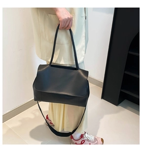 Detail of minimalist black tote bag featuring leather texture and adjustable shoulder strap