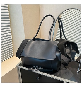 Detail of black faux leather tote bag with wide strap on a reflective cabinet setup