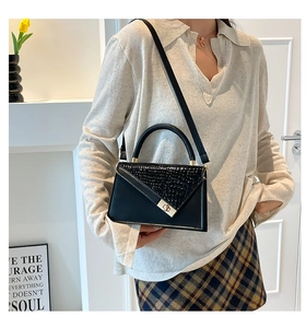 Close-up of black handbag with crocodile pattern flap and golden twist lock detail