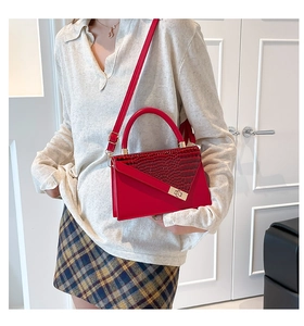 Detail of red croc-embossed flap and gold metal twist lock on structured crossbody bag