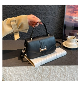 Detail of black pebbled leather crossbody bag with golden metal lock on a white book