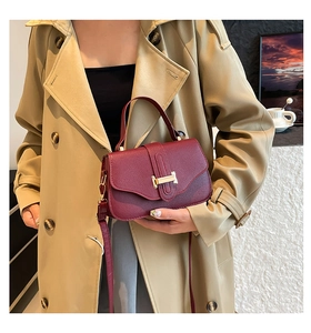 Close-up of burgundy lychee leather handbag with a gold H-shaped clasp on a trench coat
