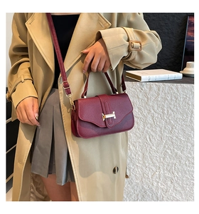 Detail of burgundy textured leather bag with iconic golden H-shaped clasp for women