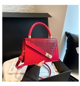 Detail of red trapezoid handbag with crocodile texture, gold lock, and top handle