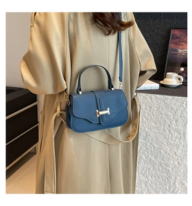 Blue lychee grain leather crossbody bag with a golden H-clasp on a beige trench coat
