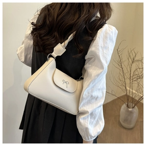 Sac sous le bras beige chic avec nœud argenté, porté dans un décor intérieur minimaliste