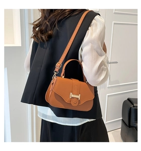 Detail shot of tan leather crossbody bag with gold buckle on a model for scale