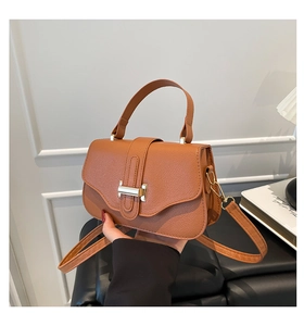 Detail of caramel brown litchi grain faux leather bag with gold metal clasp and top handle