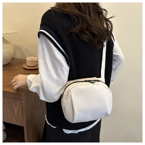 Detail of cream nylon crossbody moon bag with black zippers and adjustable strap