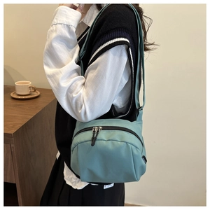 Lifestyle shot of light teal nylon crossbody bag with dual zippers and minimalist design
