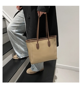 Close-up of beige tote bag with brown straps styled with a classic black coat