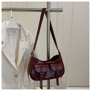 Detail of dark red leather shoulder bag featuring dual front pockets and metal buckles