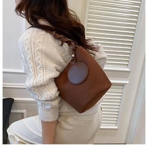 Detail view of dark brown faux suede bucket bag with braided strap and circular accents