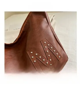 Detail von Silbernieten in M-Form auf braunem Leder an der Schultertasche mit Lychee-Struktur