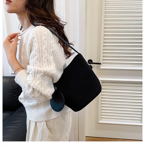 Détail du sac seau noir en daim avec petit porte-monnaie rond sur un pull blanc