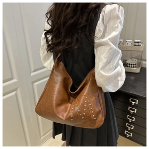 Brown vintage hobo bag with silver rivet M-logo detail shown on a female model shoulder