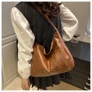 Braune Hobo-Tasche aus Leder mit M-Nietenmuster an der Schulter für den Alltag getragen
